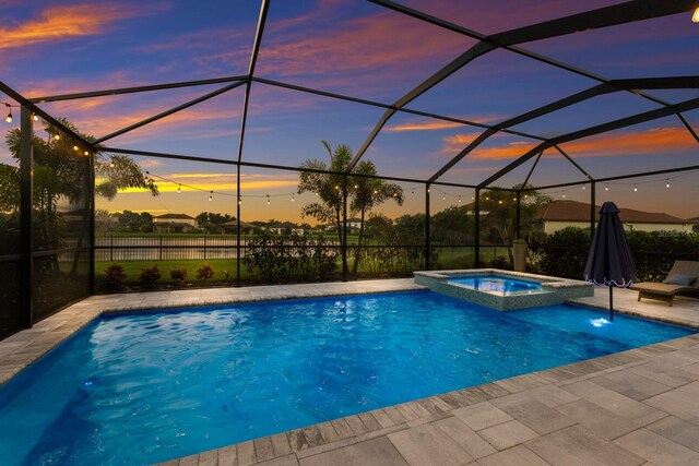 pool at dusk with glass enclosure, an in ground hot tub, and a patio area