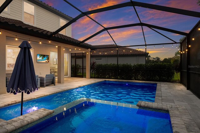 pool at dusk with a patio, an in ground hot tub, and a lanai