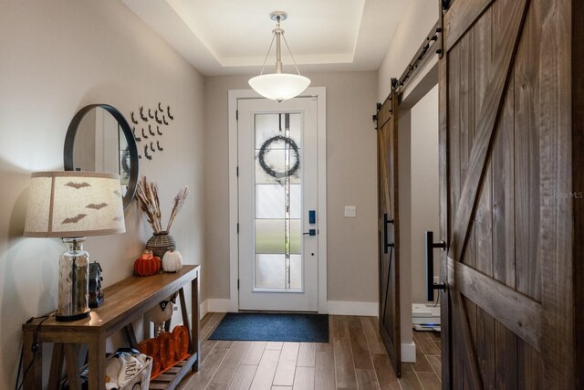 foyer with a barn door, a tray ceiling, and dark hardwood / wood-style flooring