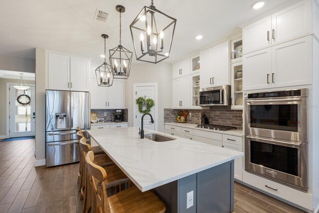 kitchen featuring an island with sink, stainless steel appliances, sink, and white cabinetry