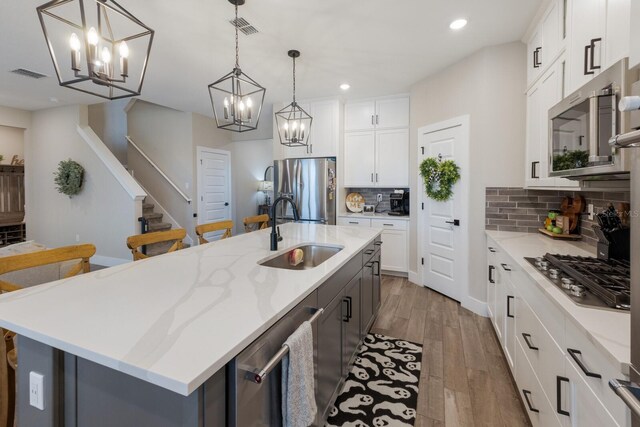 kitchen with appliances with stainless steel finishes, a large island with sink, sink, and white cabinets