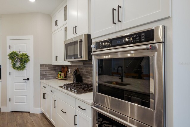 kitchen with stainless steel appliances, white cabinetry, hardwood / wood-style floors, and tasteful backsplash