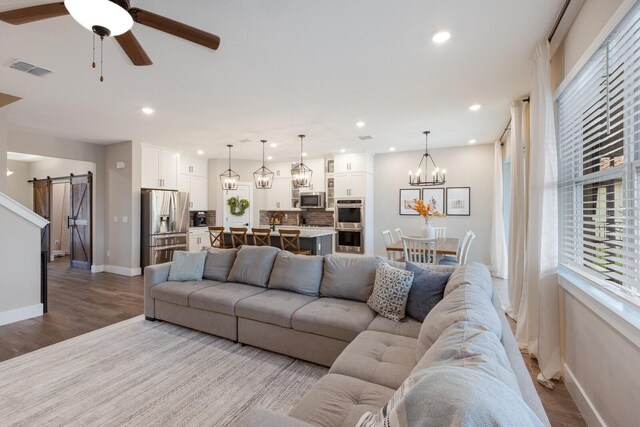 living room with light wood-type flooring, ceiling fan, and a barn door