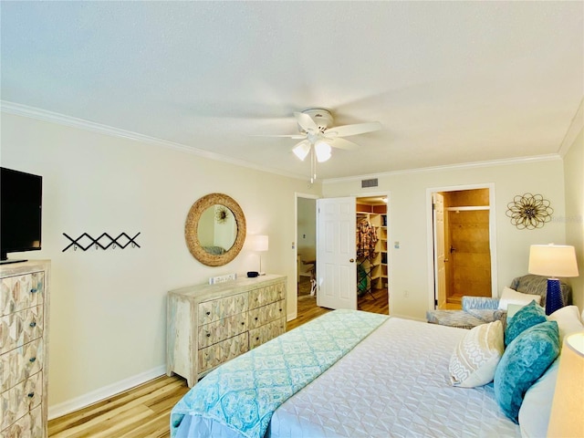 bedroom with ceiling fan, light hardwood / wood-style flooring, a walk in closet, a closet, and ornamental molding