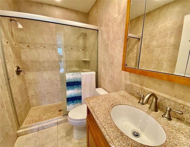 bathroom featuring tile patterned floors, an enclosed shower, toilet, vanity, and tile walls