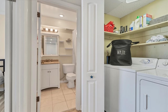 laundry area featuring washing machine and clothes dryer, sink, light tile patterned floors, and a textured ceiling