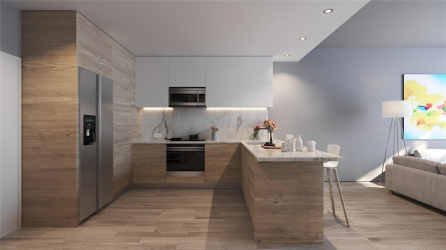 kitchen with white cabinets, kitchen peninsula, appliances with stainless steel finishes, and light wood-type flooring