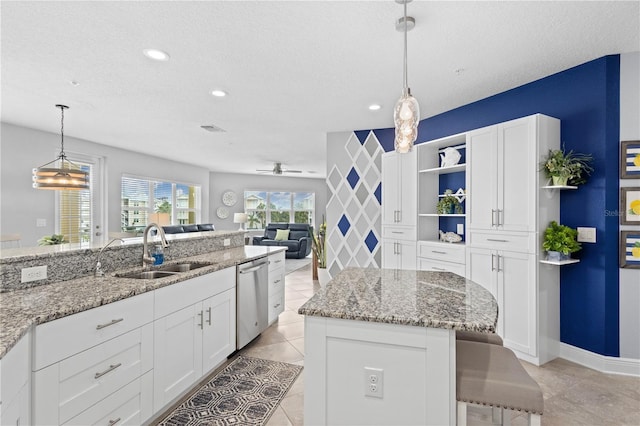 kitchen featuring hanging light fixtures, white cabinetry, light stone counters, stainless steel dishwasher, and sink