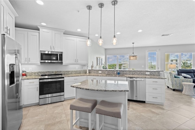 kitchen with hanging light fixtures, white cabinetry, kitchen peninsula, stainless steel appliances, and a kitchen bar