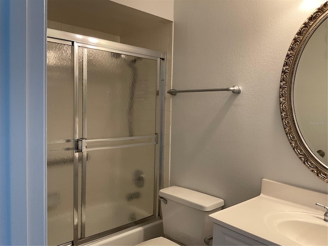 full bathroom with enclosed tub / shower combo, a textured wall, vanity, and toilet