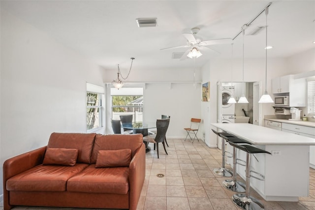 tiled living room with ceiling fan and stacked washer / dryer