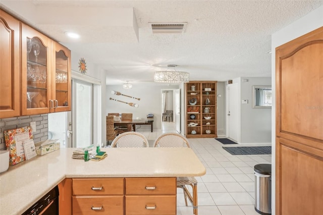 kitchen featuring decorative backsplash, a breakfast bar, kitchen peninsula, light tile patterned floors, and a textured ceiling