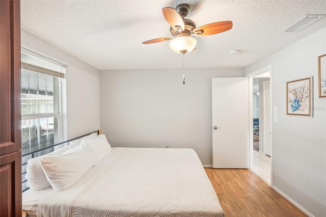 bedroom featuring light hardwood / wood-style flooring, a textured ceiling, and ceiling fan