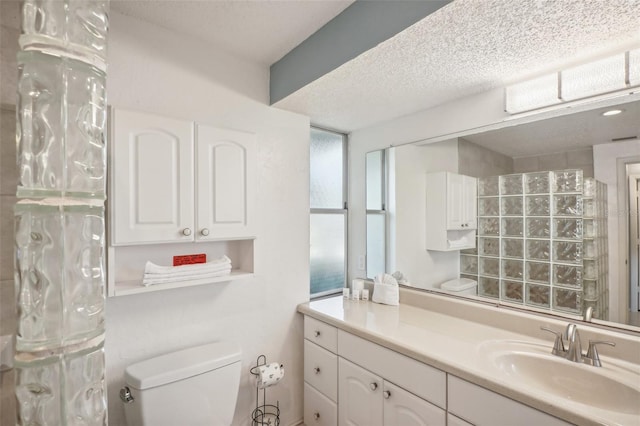 bathroom featuring a textured ceiling, walk in shower, vanity, and toilet