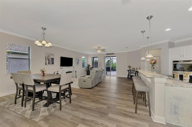 dining room with ceiling fan, ornamental molding, sink, and light wood-type flooring