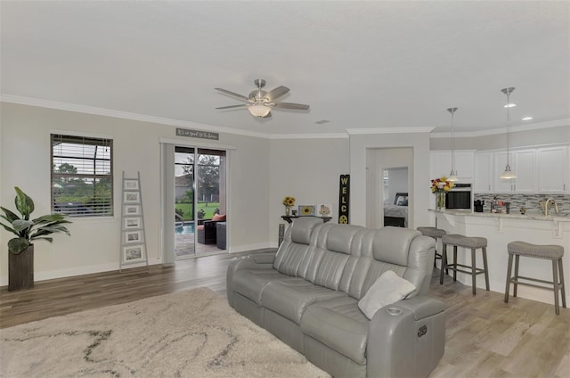 living room featuring light hardwood / wood-style floors, ornamental molding, sink, and ceiling fan