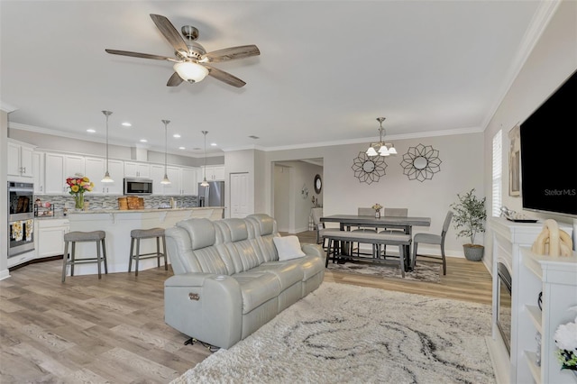 living room with ornamental molding, ceiling fan with notable chandelier, and light hardwood / wood-style floors