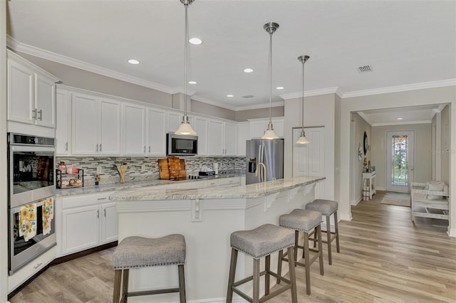 kitchen featuring pendant lighting, stainless steel appliances, light stone countertops, white cabinets, and a center island with sink