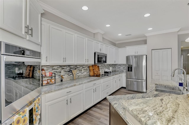 kitchen featuring sink, white cabinetry, stainless steel appliances, ornamental molding, and light stone countertops