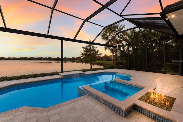 pool at dusk featuring a fire pit, glass enclosure, a water view, and an in ground hot tub