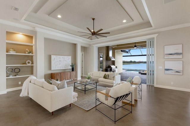 living room with a tray ceiling, built in features, a water view, and ornamental molding