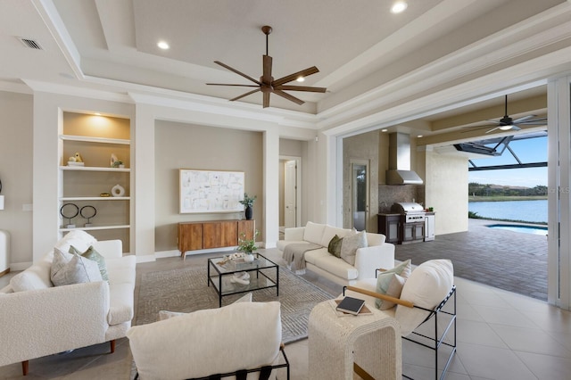 living room featuring built in features, a water view, a raised ceiling, and crown molding