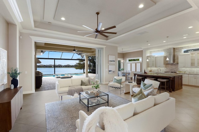 living room with a tray ceiling, sink, a water view, and ornamental molding