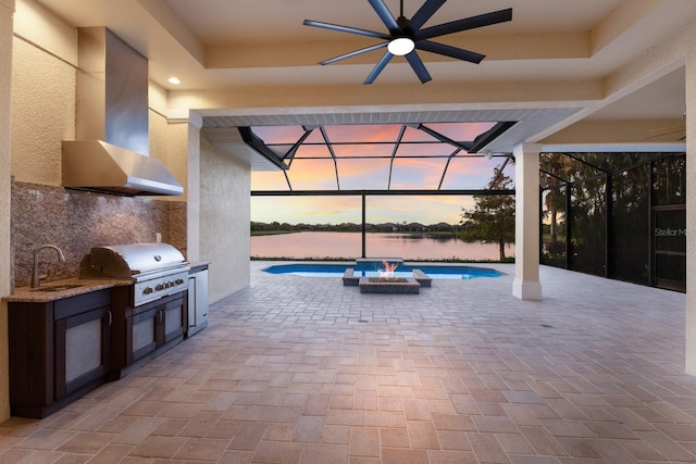 patio terrace at dusk featuring area for grilling, ceiling fan, sink, and a water view