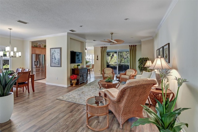 living room featuring hardwood / wood-style floors, ceiling fan with notable chandelier, crown molding, and a textured ceiling