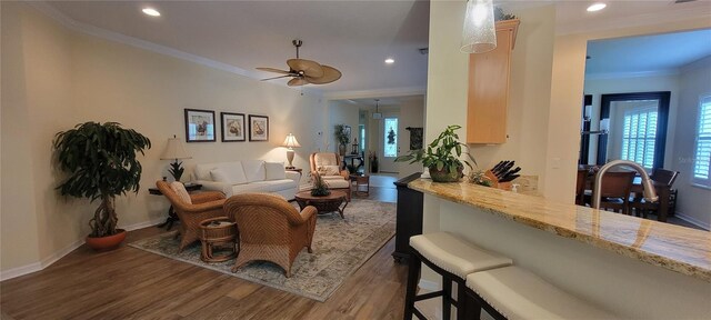 living area featuring a ceiling fan, baseboards, recessed lighting, wood finished floors, and ornamental molding