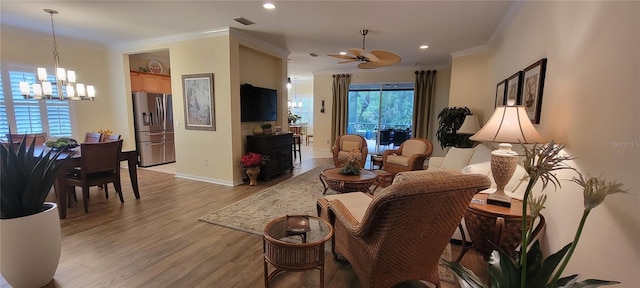 living area featuring visible vents, ornamental molding, light wood finished floors, and ceiling fan with notable chandelier