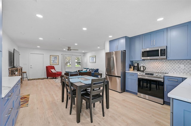 kitchen featuring tasteful backsplash, ceiling fan, stainless steel appliances, blue cabinetry, and light hardwood / wood-style flooring