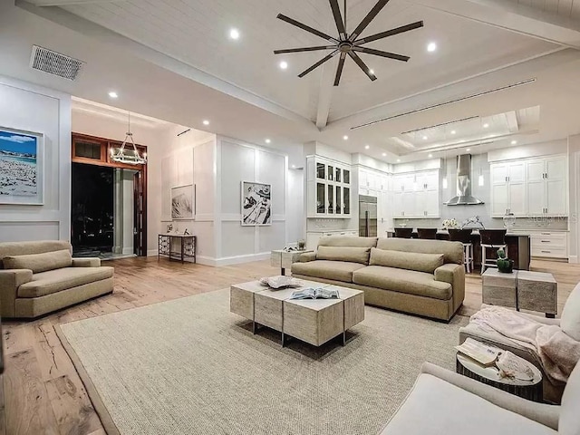 living room with ceiling fan, beamed ceiling, light wood-type flooring, and a raised ceiling