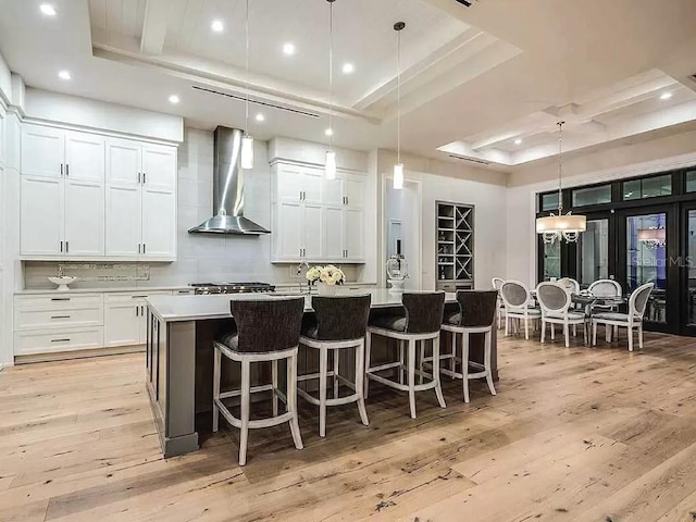 kitchen featuring wall chimney range hood, decorative light fixtures, a large island, and a raised ceiling