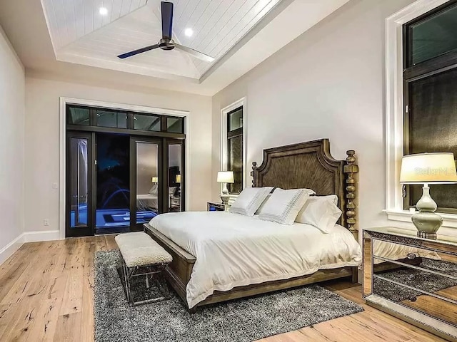 bedroom featuring access to outside, ceiling fan, hardwood / wood-style flooring, and a raised ceiling