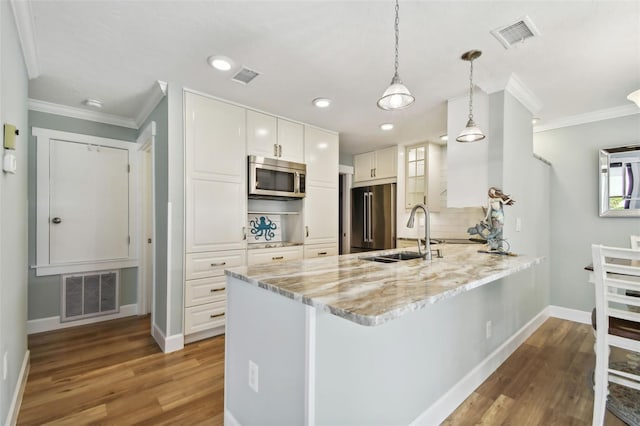 kitchen featuring decorative backsplash, hardwood / wood-style flooring, kitchen peninsula, white cabinetry, and appliances with stainless steel finishes