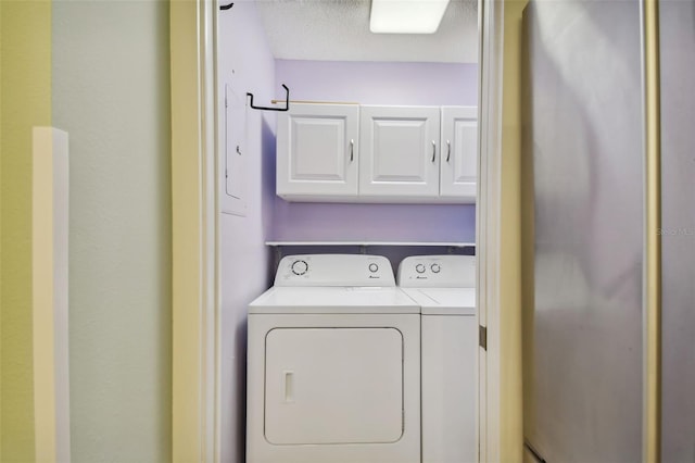 clothes washing area with a textured ceiling, washing machine and dryer, and cabinets