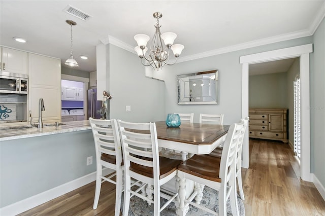 dining space with crown molding, a notable chandelier, sink, and light wood-type flooring