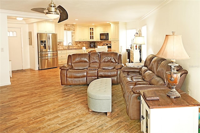 living room featuring ceiling fan, decorative columns, light hardwood / wood-style flooring, crown molding, and sink