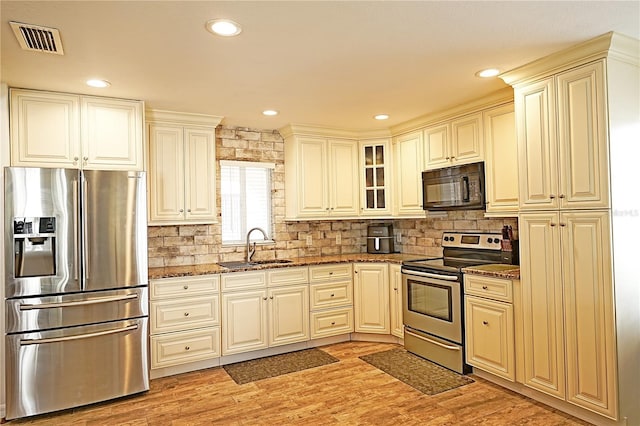 kitchen featuring tasteful backsplash, sink, light wood-type flooring, stainless steel appliances, and dark stone countertops