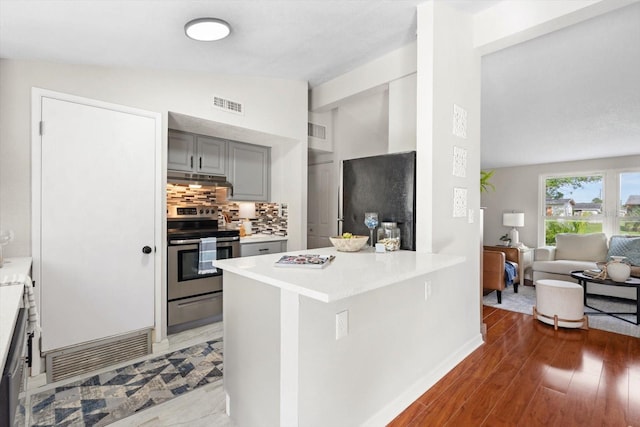 kitchen featuring black fridge, lofted ceiling, kitchen peninsula, stainless steel range with electric cooktop, and dark hardwood / wood-style flooring