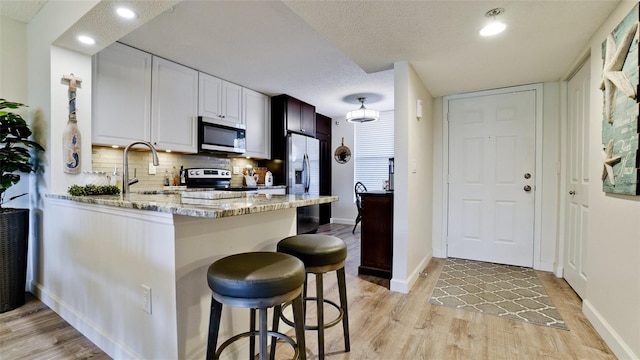 kitchen with decorative backsplash, a kitchen bar, kitchen peninsula, stainless steel appliances, and sink