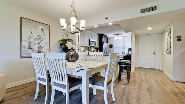 dining room with an inviting chandelier, a textured ceiling, and light hardwood / wood-style flooring