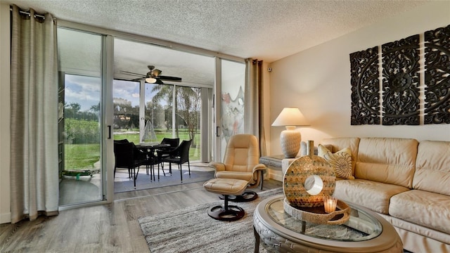 living room featuring ceiling fan, expansive windows, wood-type flooring, and a textured ceiling