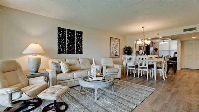 living room featuring wood-type flooring, a textured ceiling, and a notable chandelier