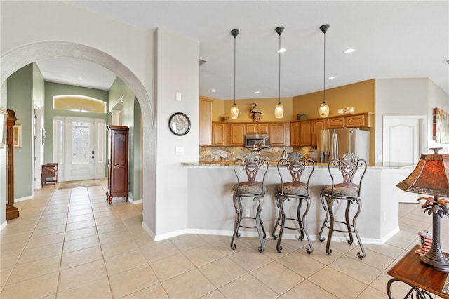 kitchen featuring tasteful backsplash, kitchen peninsula, appliances with stainless steel finishes, light tile patterned floors, and decorative light fixtures