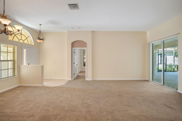 empty room with light colored carpet, an inviting chandelier, and a wealth of natural light