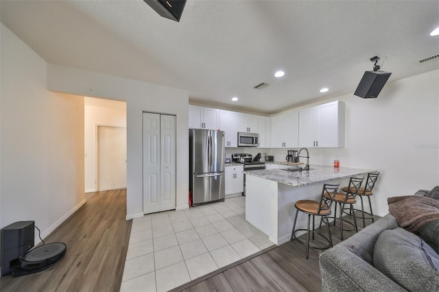 kitchen featuring sink, white cabinets, kitchen peninsula, light hardwood / wood-style flooring, and appliances with stainless steel finishes