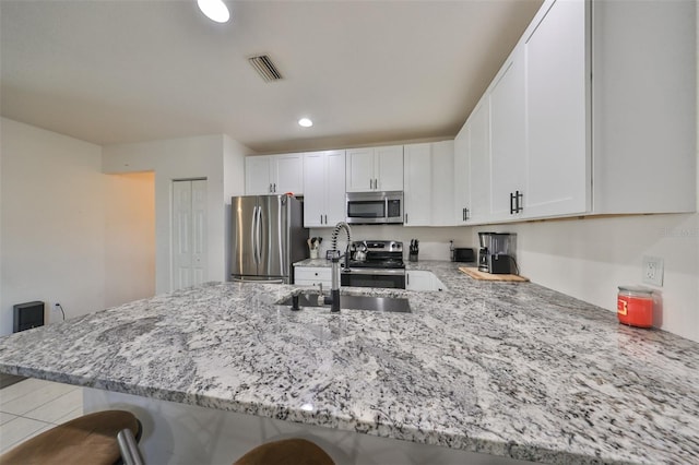 kitchen featuring stainless steel appliances, white cabinetry, kitchen peninsula, and a kitchen bar