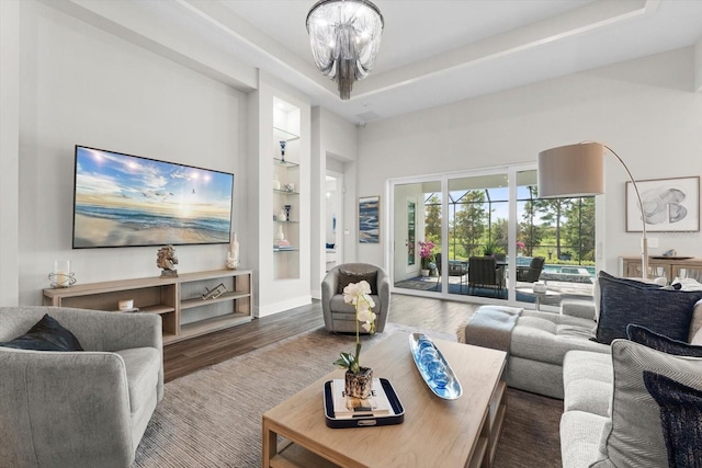 living room featuring a raised ceiling, built in shelves, wood-type flooring, and an inviting chandelier